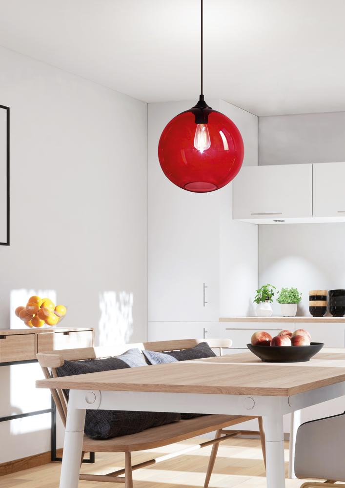 Suspension rouge en verre illuminée au-dessus d'une table en bois dans une cuisine blanche.