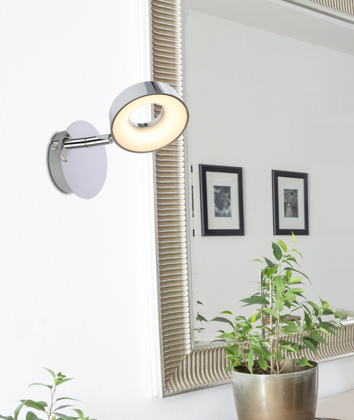Applique chromée allumée fixée au mur près d'un miroir et d'une plante verte
