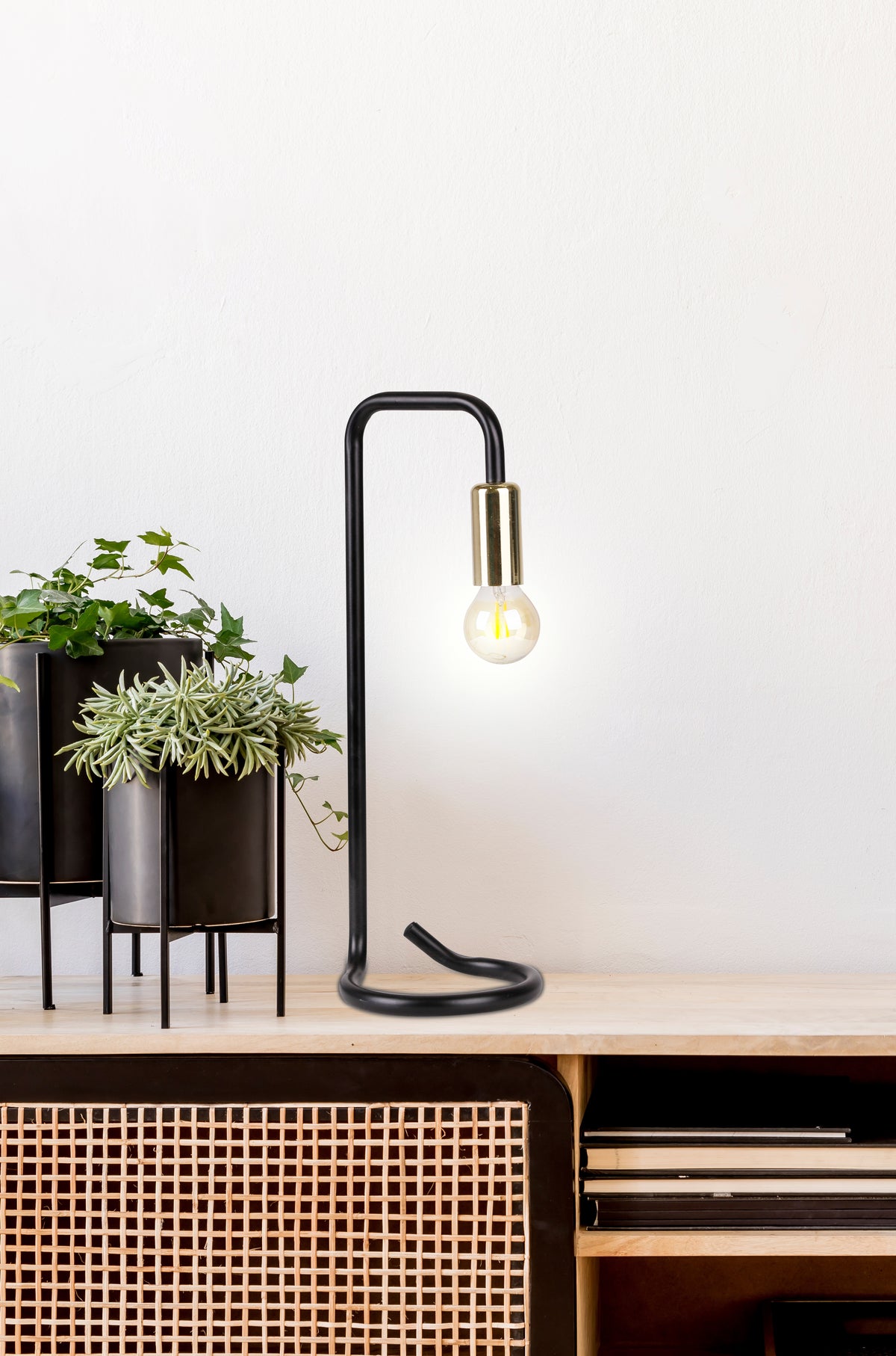 Lampe allumée posée sur un meuble en bois, près de plantes vertes.