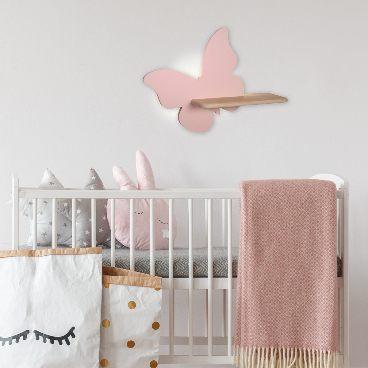 Mise en ambiance chambre d'enfant : applique papillon rose au-dessus d'un lit bébé avec peluches.