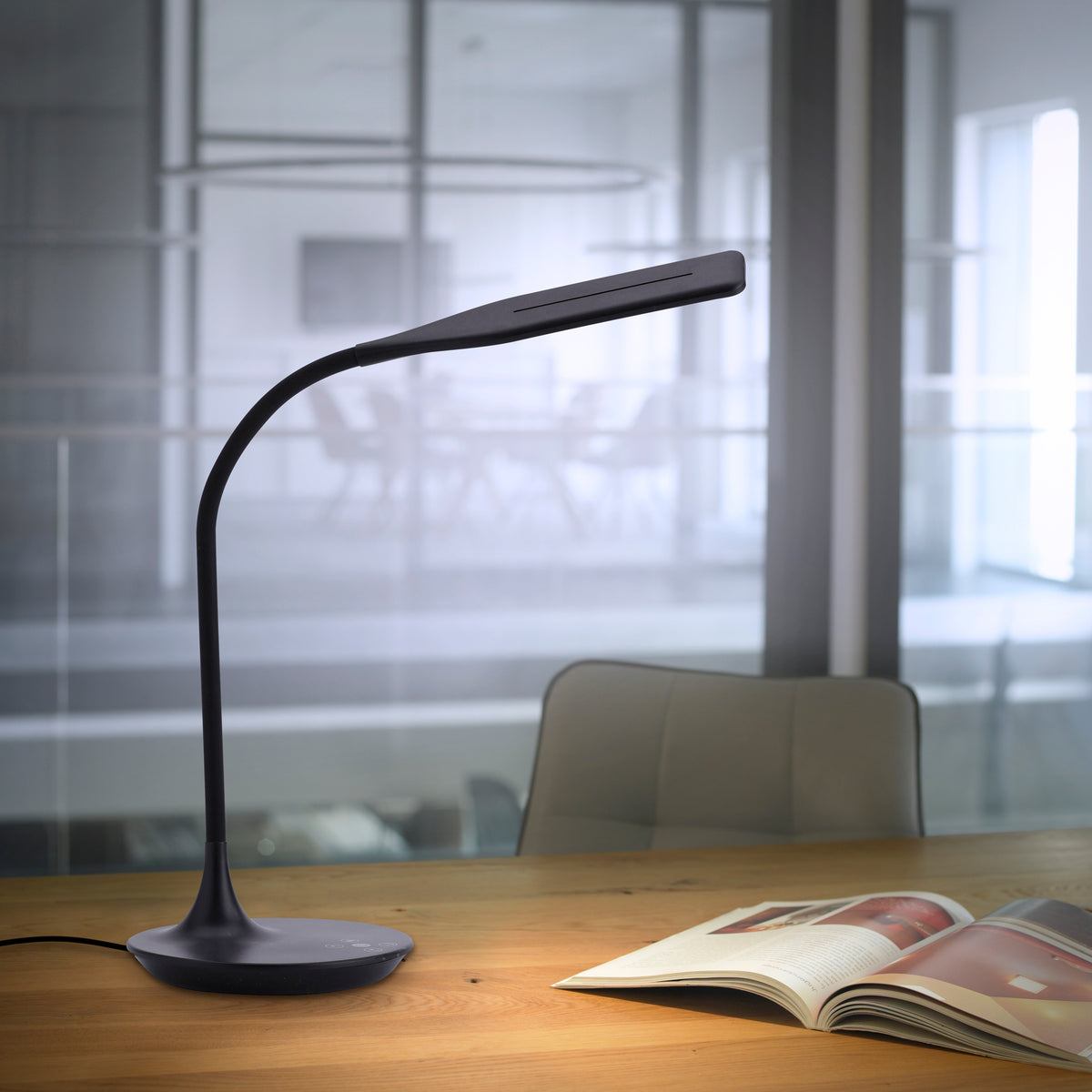 Mise en ambiance sur bureau en bois, lampe allumée et magazine ouvert au premier plan.