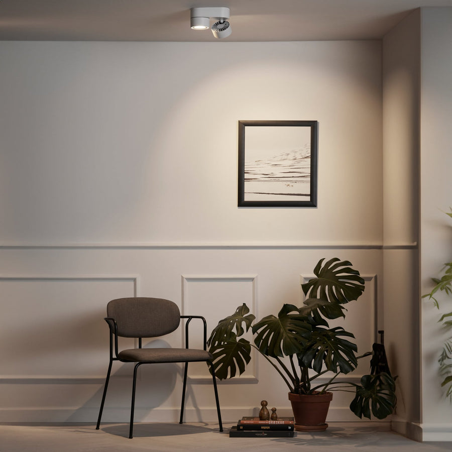 Spot plafond allumé projetant une lumière chaude sur un mur et un cadre.