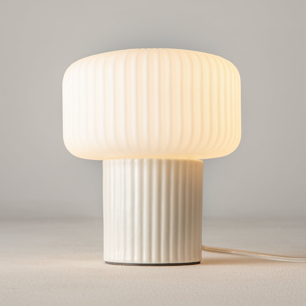 Lampe allumée posée sur surface beige, câble transparent visible à droite, lumière chaude.