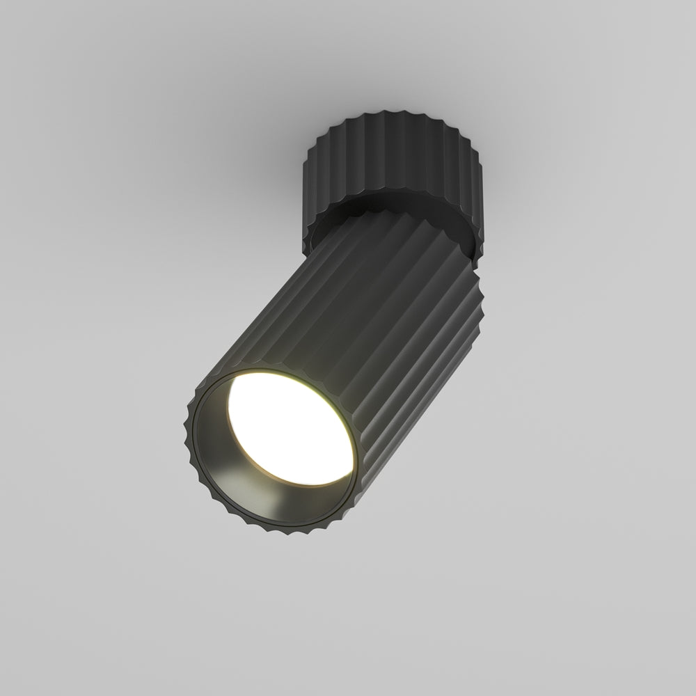 Spot plafonnier cylindrique noir nervuré orientable, vu de trois quarts sur fond gris