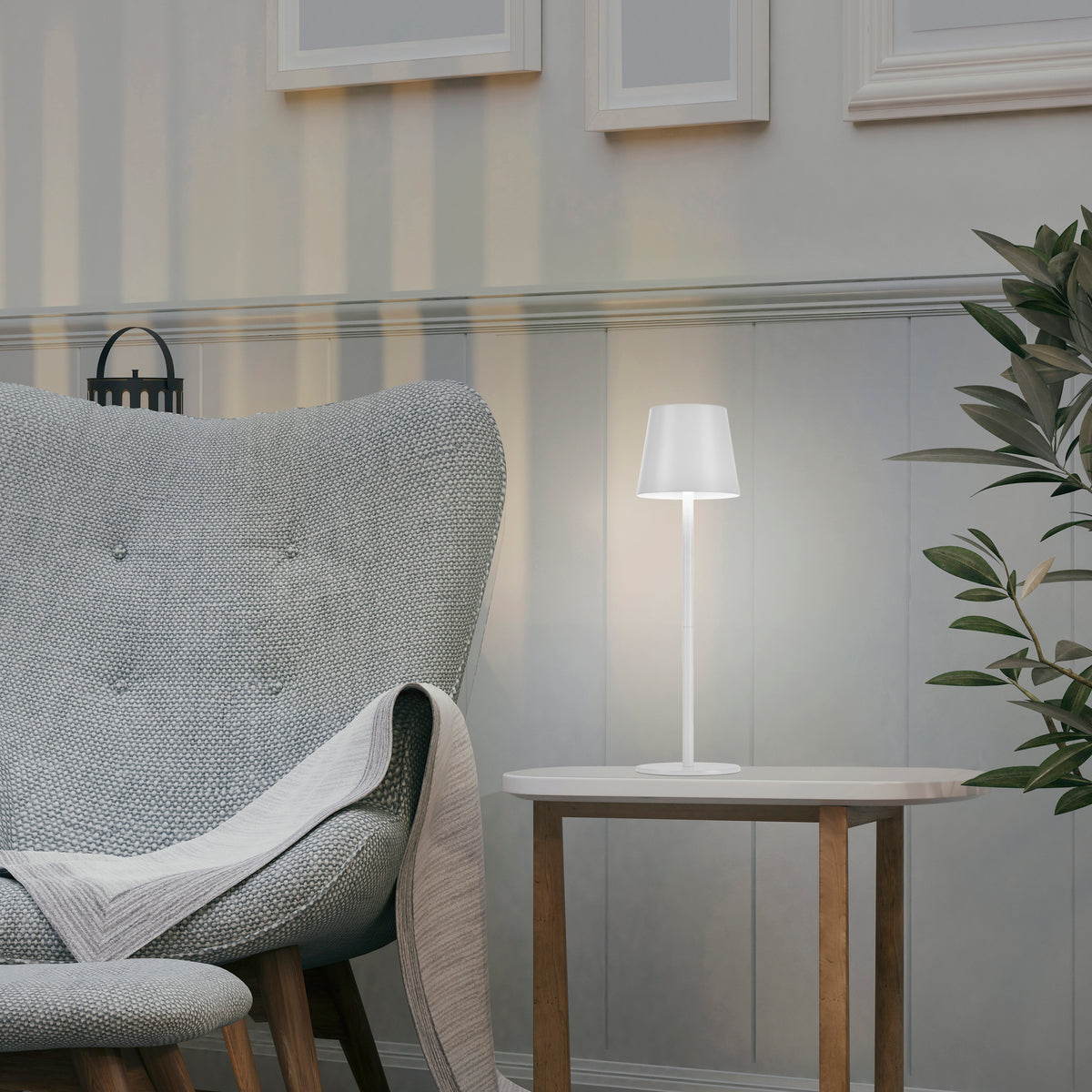 Lampe blanche allumée posée sur une table d'appoint près d'un fauteuil gris.