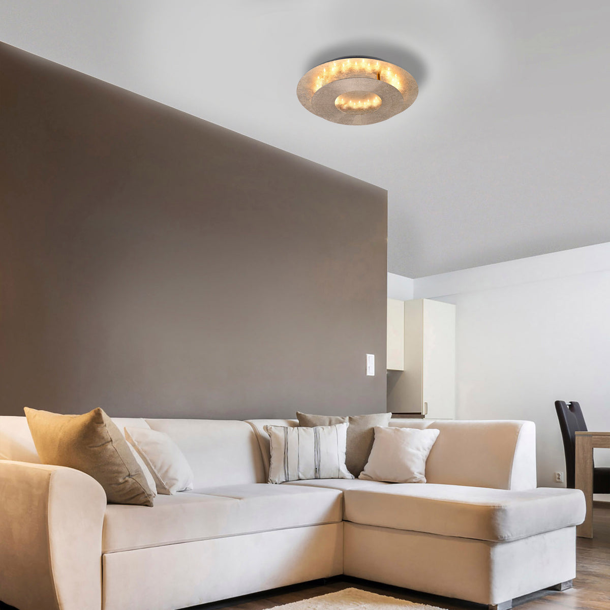 Mise en ambiance d'un salon moderne avec le plafonnier allumé au-dessus du canapé beige.