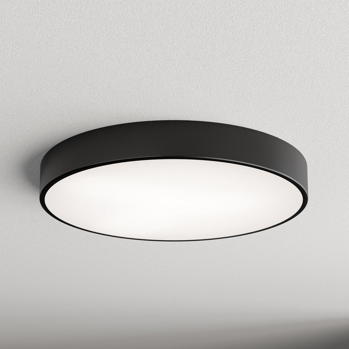 Plafonnier rond noir fixé au plafond, diffuseur blanc lumineux, vue de face.