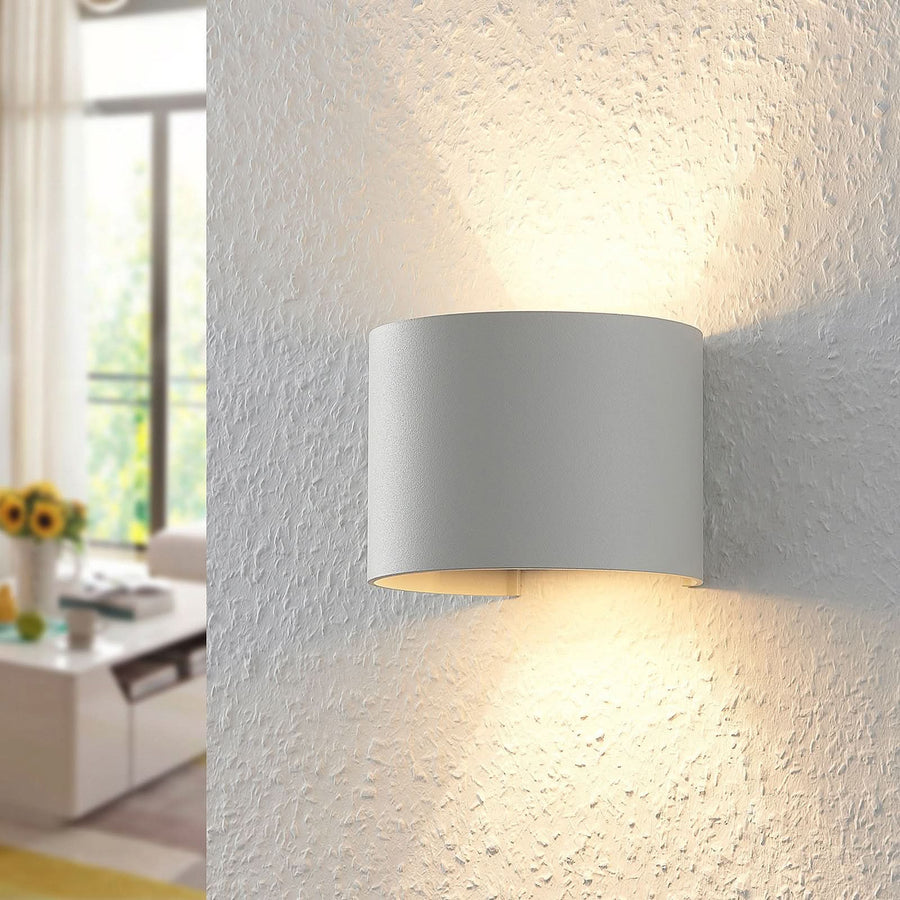 Gros plan de l’applique allumée sur un mur texturé, lumière chaude diffusée.