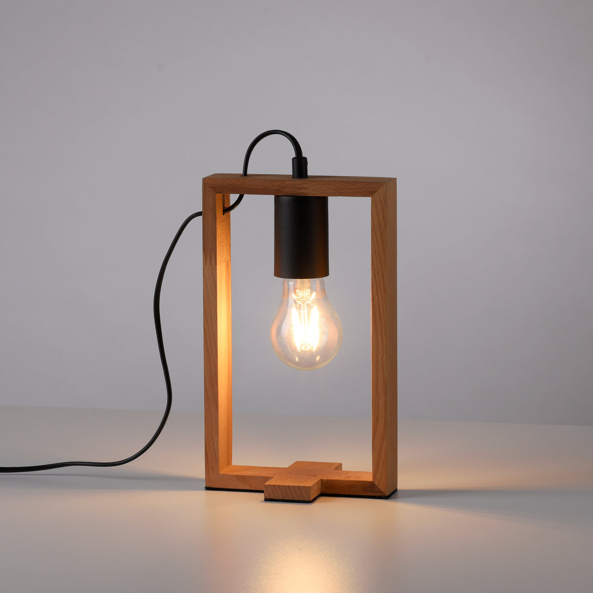Lampe en bois allumée posée sur surface blanche, ampoule Edison brillante et câble noir.