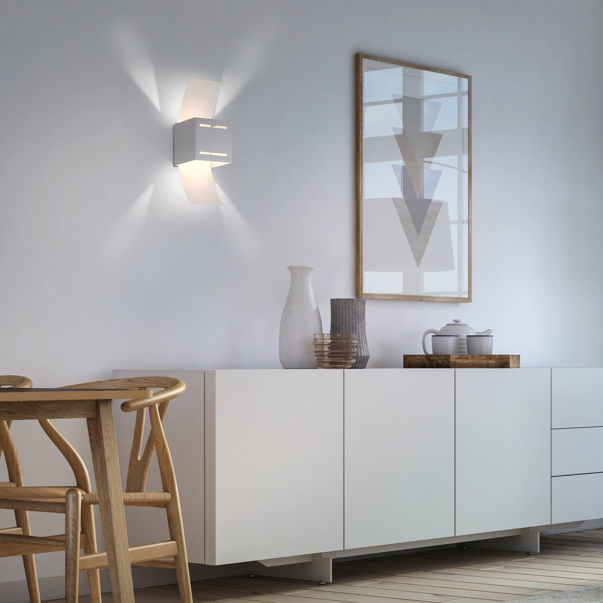 Mise en ambiance dans un salon clair, applique allumée sur mur blanc, buffet et cadre