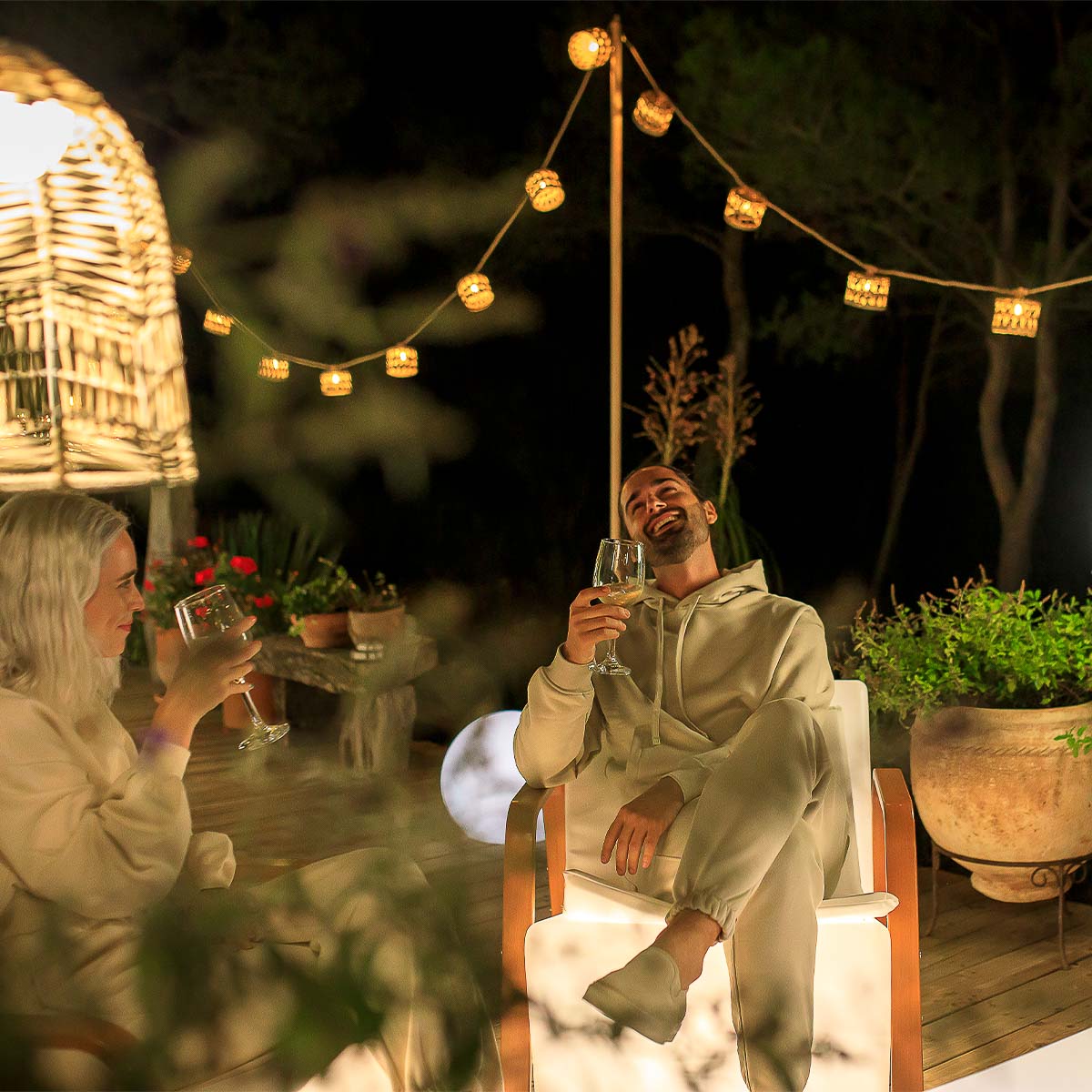 Mise en ambiance nocturne, couple trinquant sous la guirlande dans un jardin