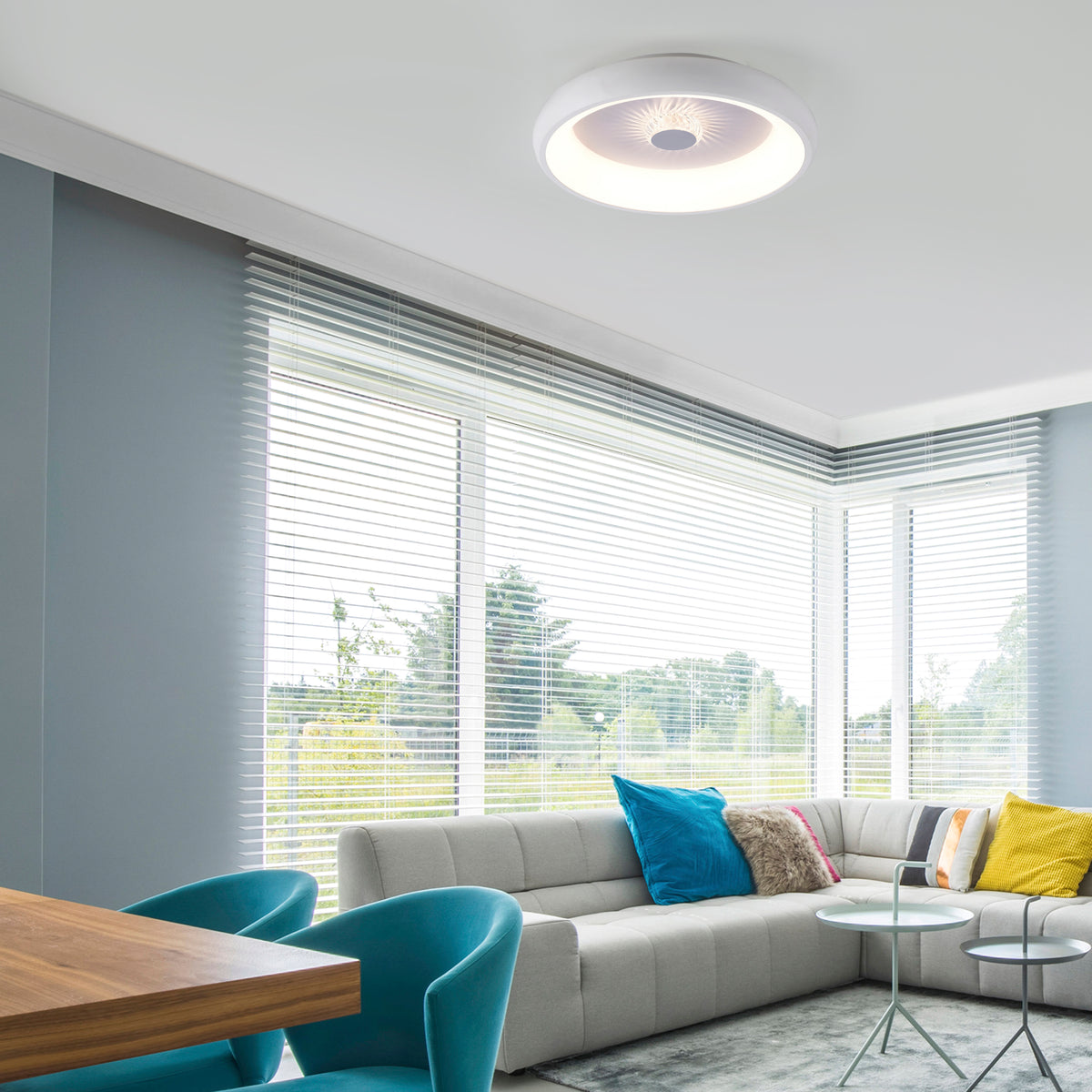 Mise en ambiance du plafonnier allumé dans un salon moderne aux grandes fenêtres et canapé gris.
