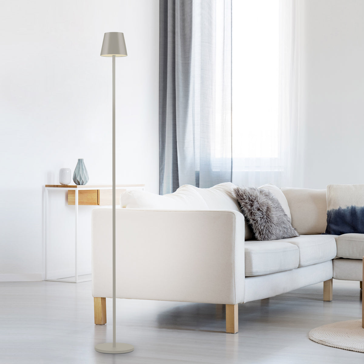 Mise en ambiance dans un salon lumineux, lampe derrière un canapé beige et rideaux.