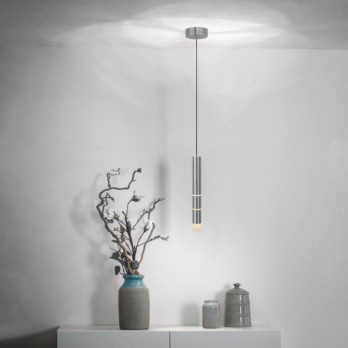 Mise en ambiance de la suspension allumée dans un intérieur épuré avec vase et poteries.