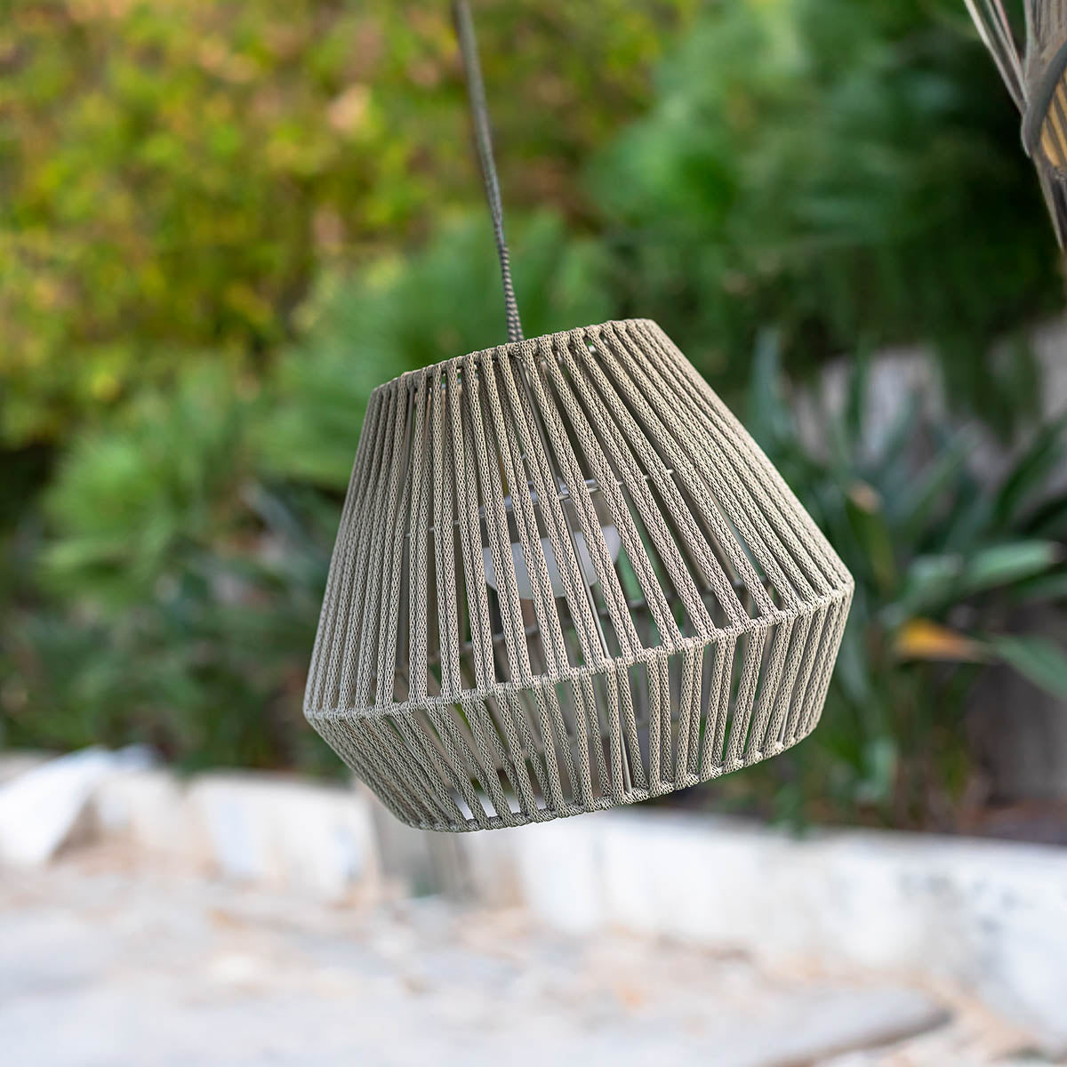 Luminaire beige vu de face sur fond de feuillage vert flou