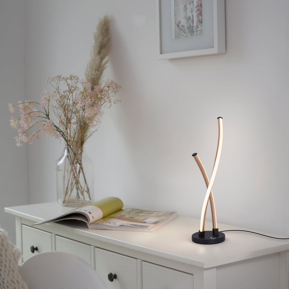 Lampe dorée posée sur un meuble blanc, éclairant une ambiance douce avec vase et magazine.