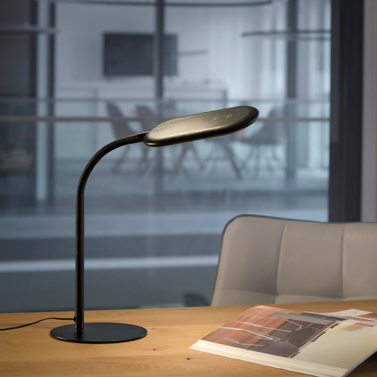Mise en ambiance sur table en bois, lampe allumée devant un bureau vitré.