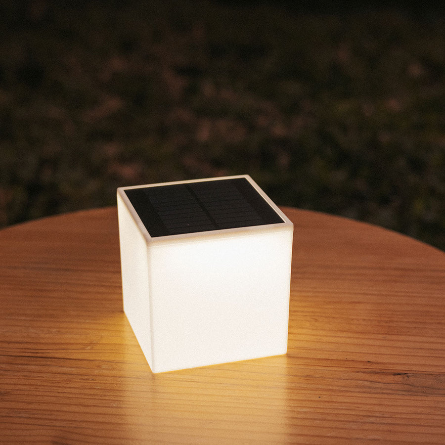 Luminaire posé sur table en bois le soir, halo diffus dans le jardin