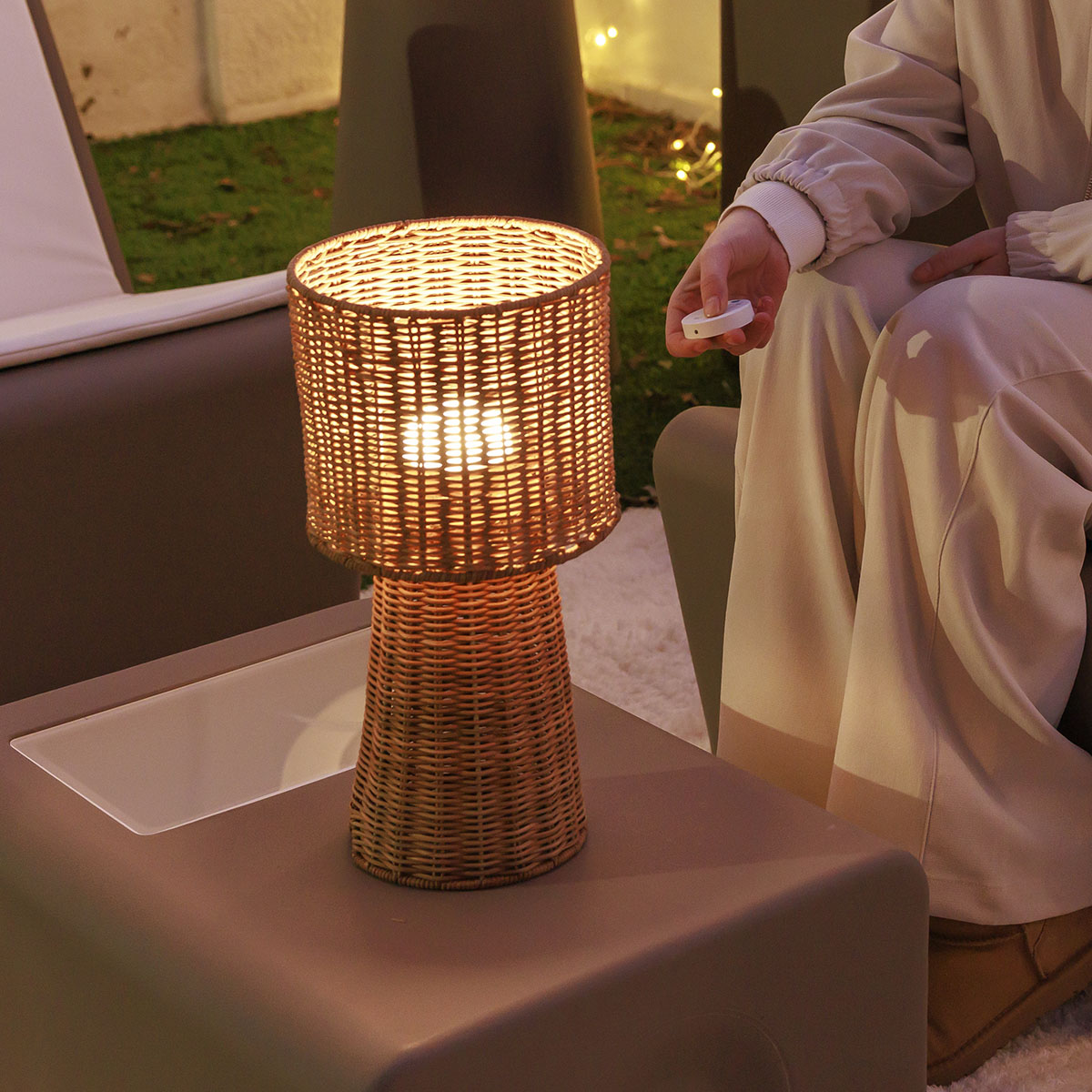 Lampe allumée posée sur une table basse, femme tenant une télécommande blanche