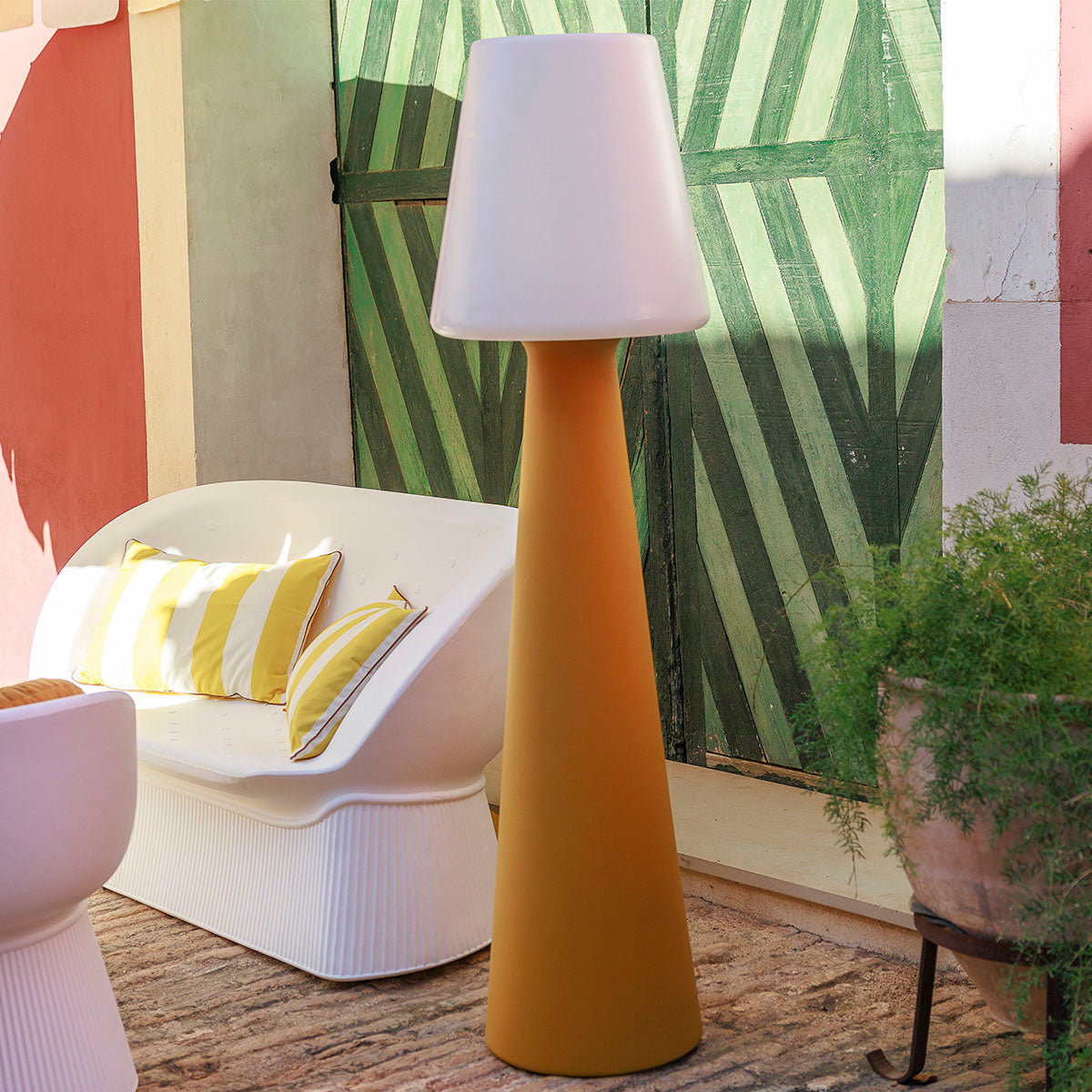 Lampadaire jaune moutarde dans une cour colorée près d'un canapé blanc et d'un mur peint.