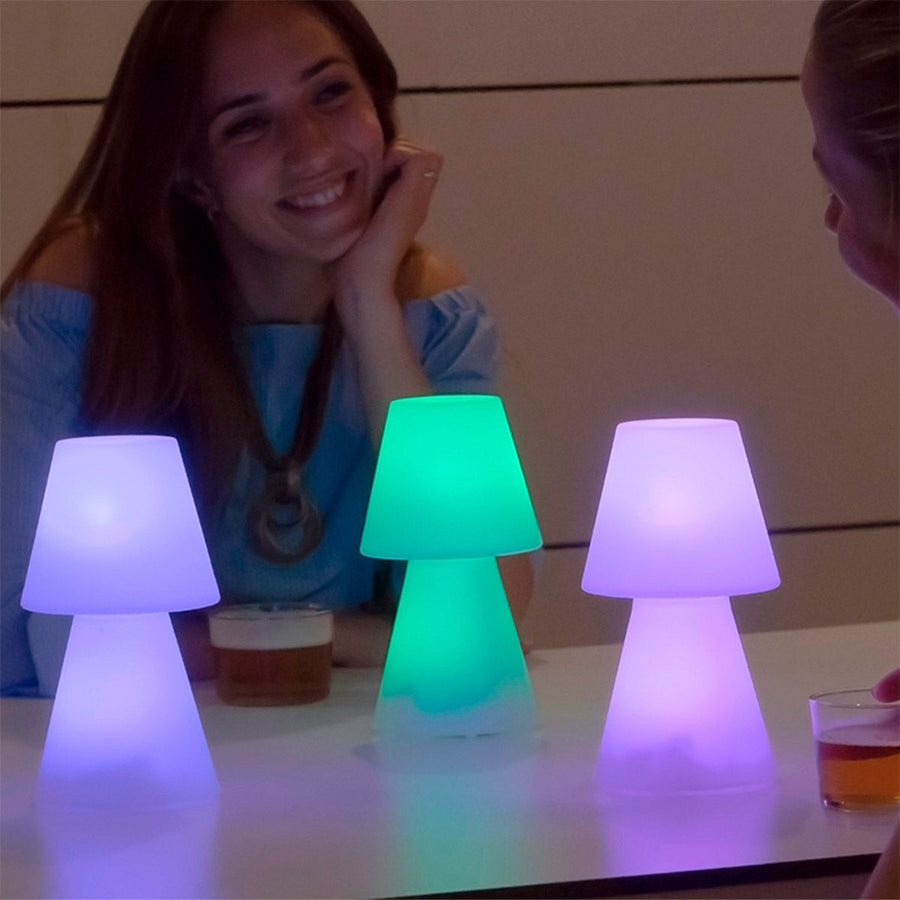 Trois lampes à poser colorées sur une table, une femme souriante en arrière-plan.