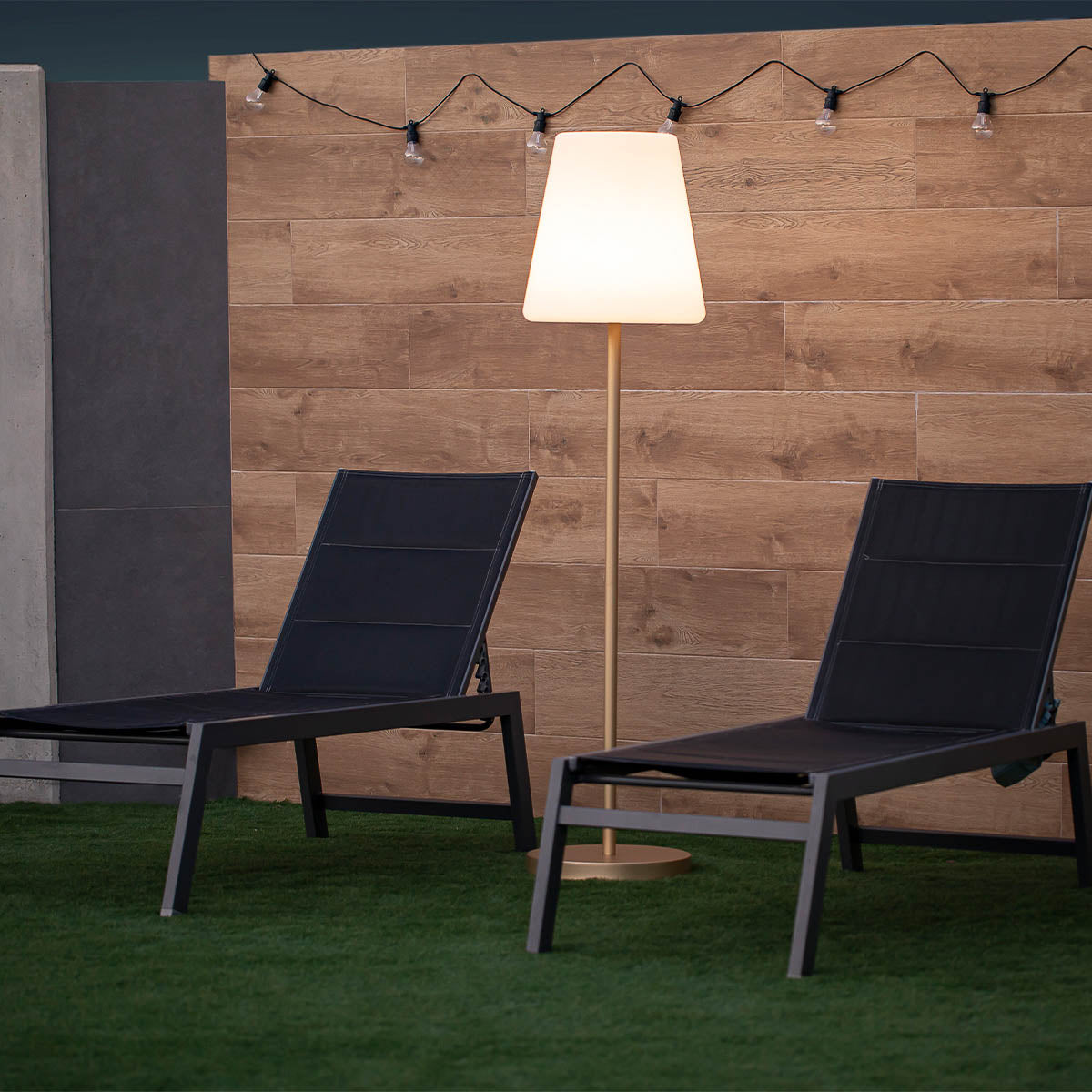 Lampadaire doré entre deux chaises longues noires, devant un mur de bois.