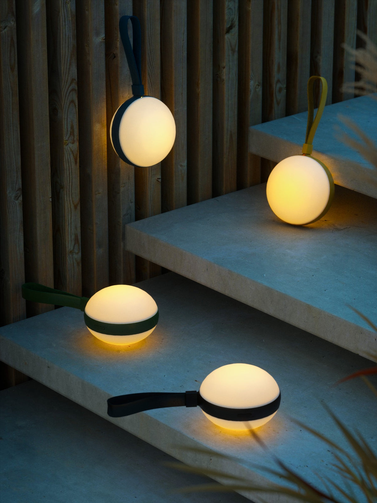 Plusieurs lampes suspendues et posées sur des marches en béton, ambiance extérieure.