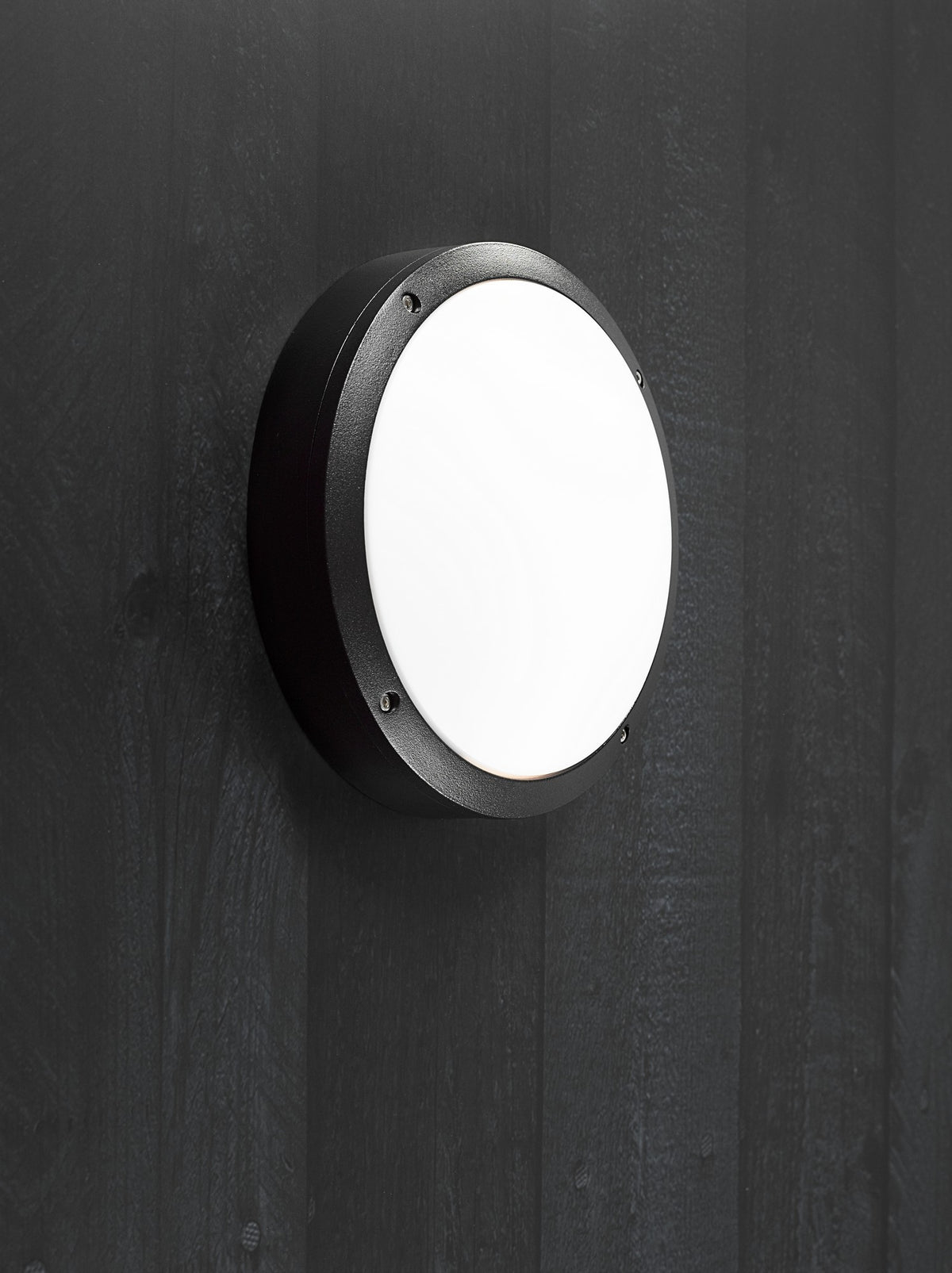 Luminaire rond noir installé sur une paroi en bois vertical, éclairant vers l'extérieur.
