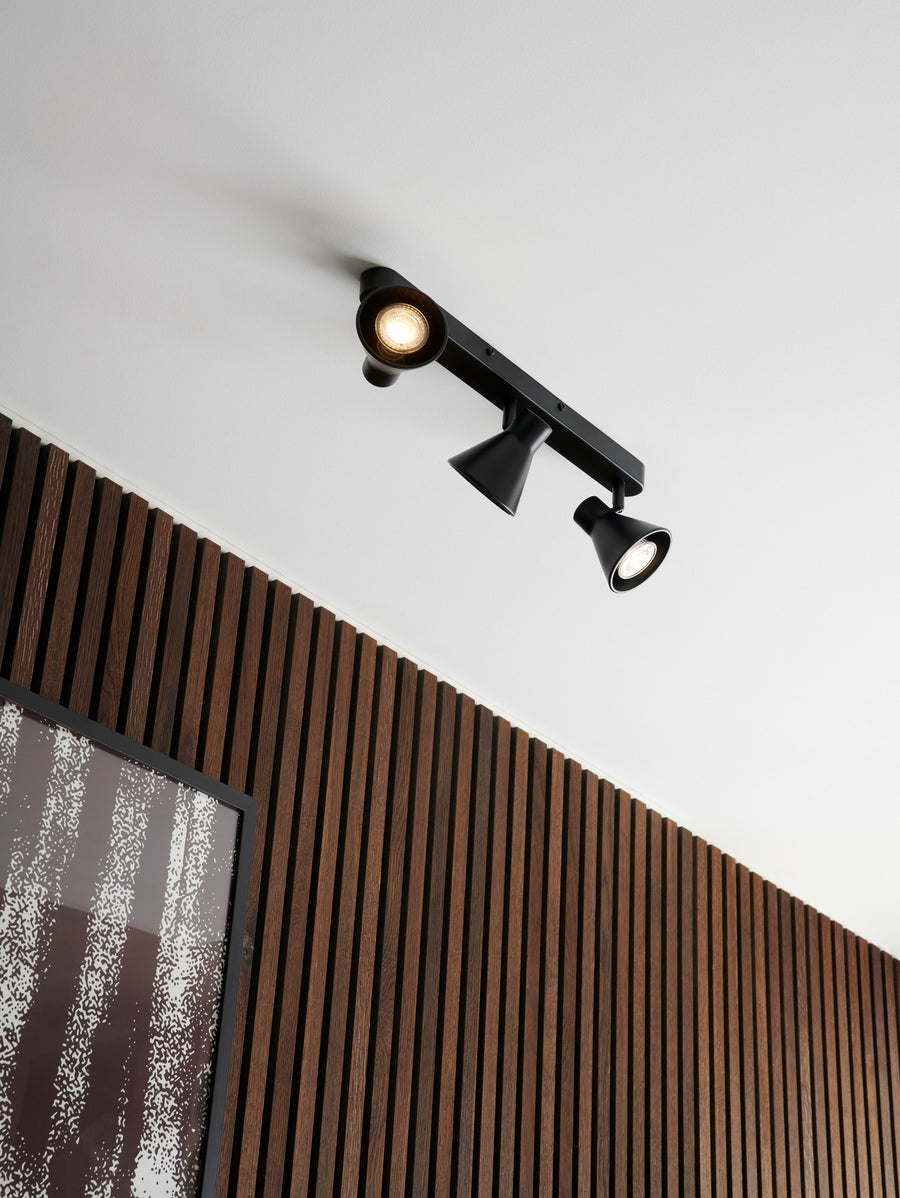 Plafonnier noir installé au plafond devant un mur à lattes de bois.