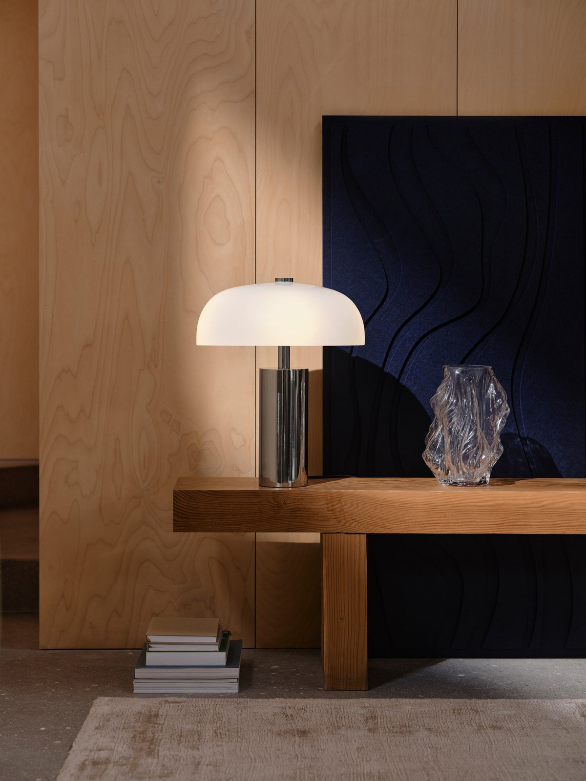 Mise en ambiance avec lampe allumée sur console en bois et vase en verre.