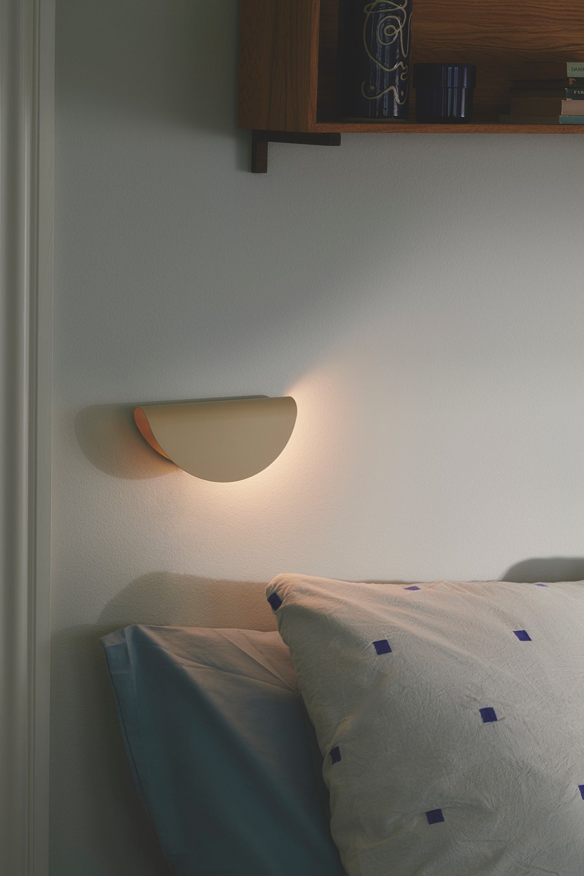 Mise en ambiance nocturne : applique murale allumée au-dessus d'un lit, lumière chaude.