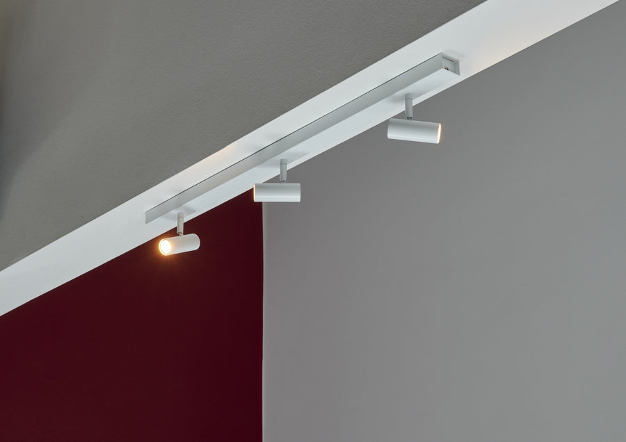 Vue en situation du rail blanc fixé au plafond, un spot allumé éclairant le mur.