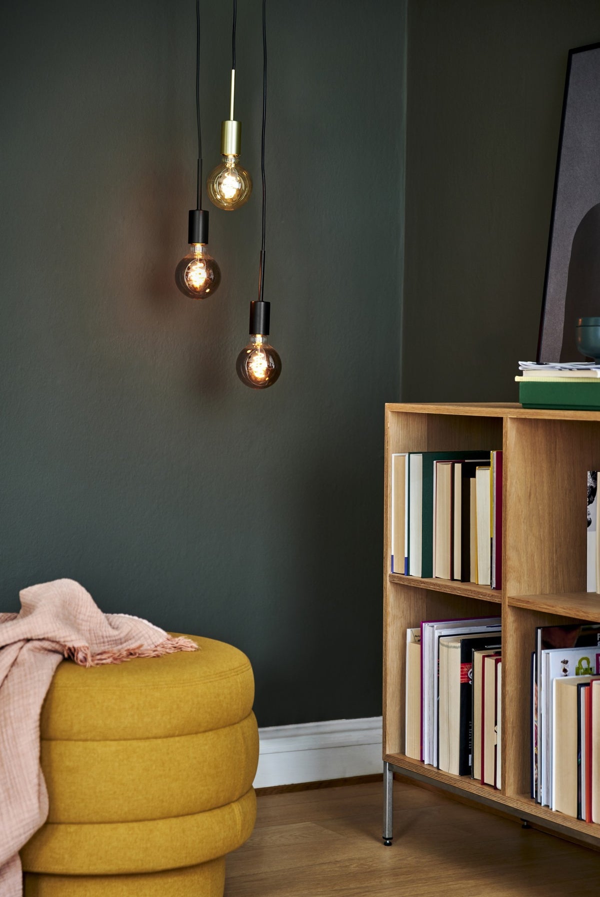 Mise en ambiance sur mur vert foncé, étagère en bois et pouf jaune moutarde