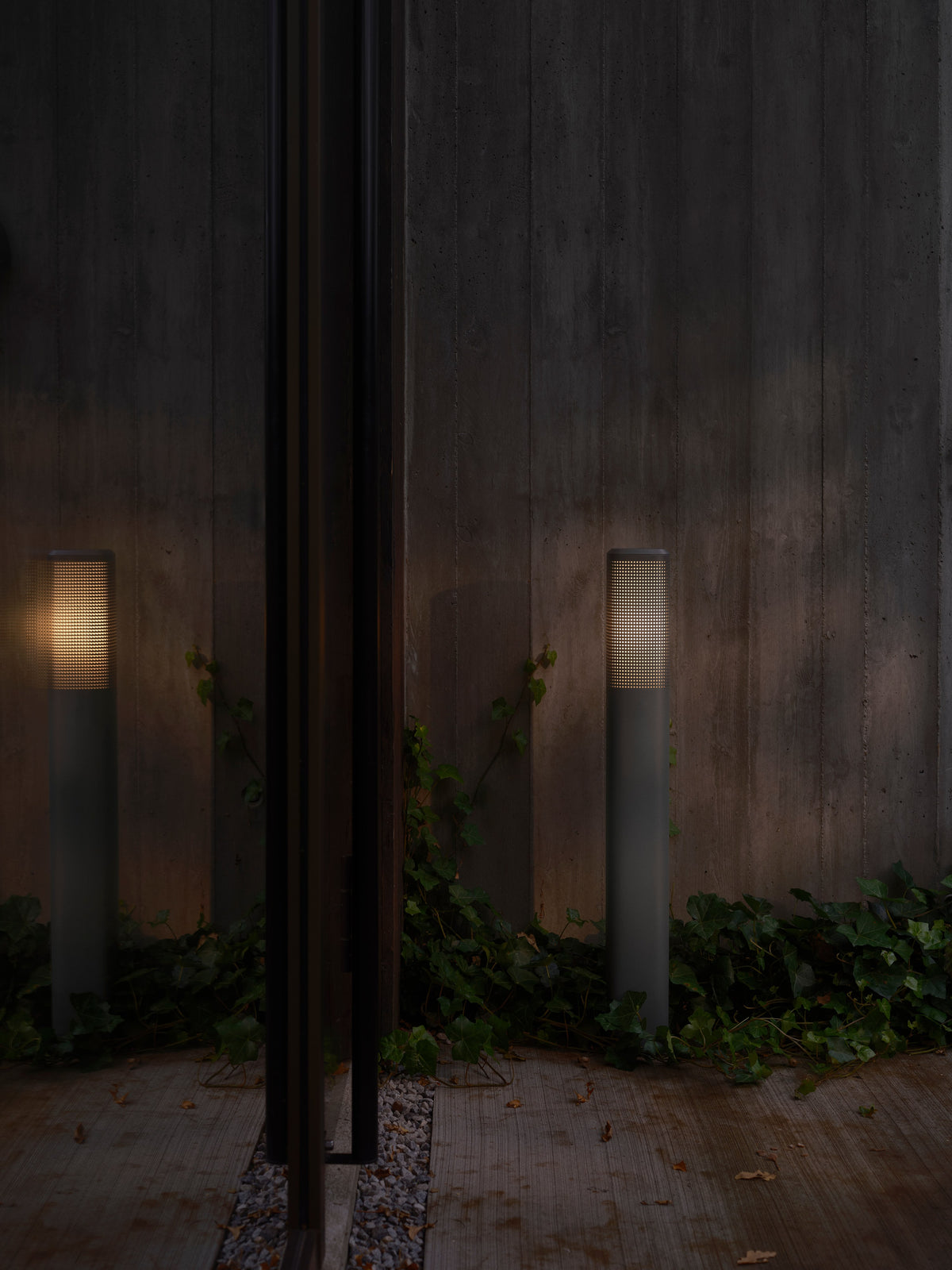 Mise en ambiance nocturne, deux bornes allumées devant mur béton et lierre