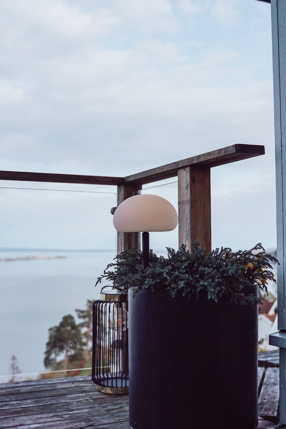 Lampe blanche sur une jardinière noire, terrasse en bois face à la mer.