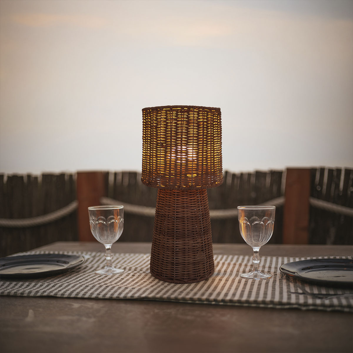 Lampe posée sur une table dressée, verres et assiettes au coucher du soleil