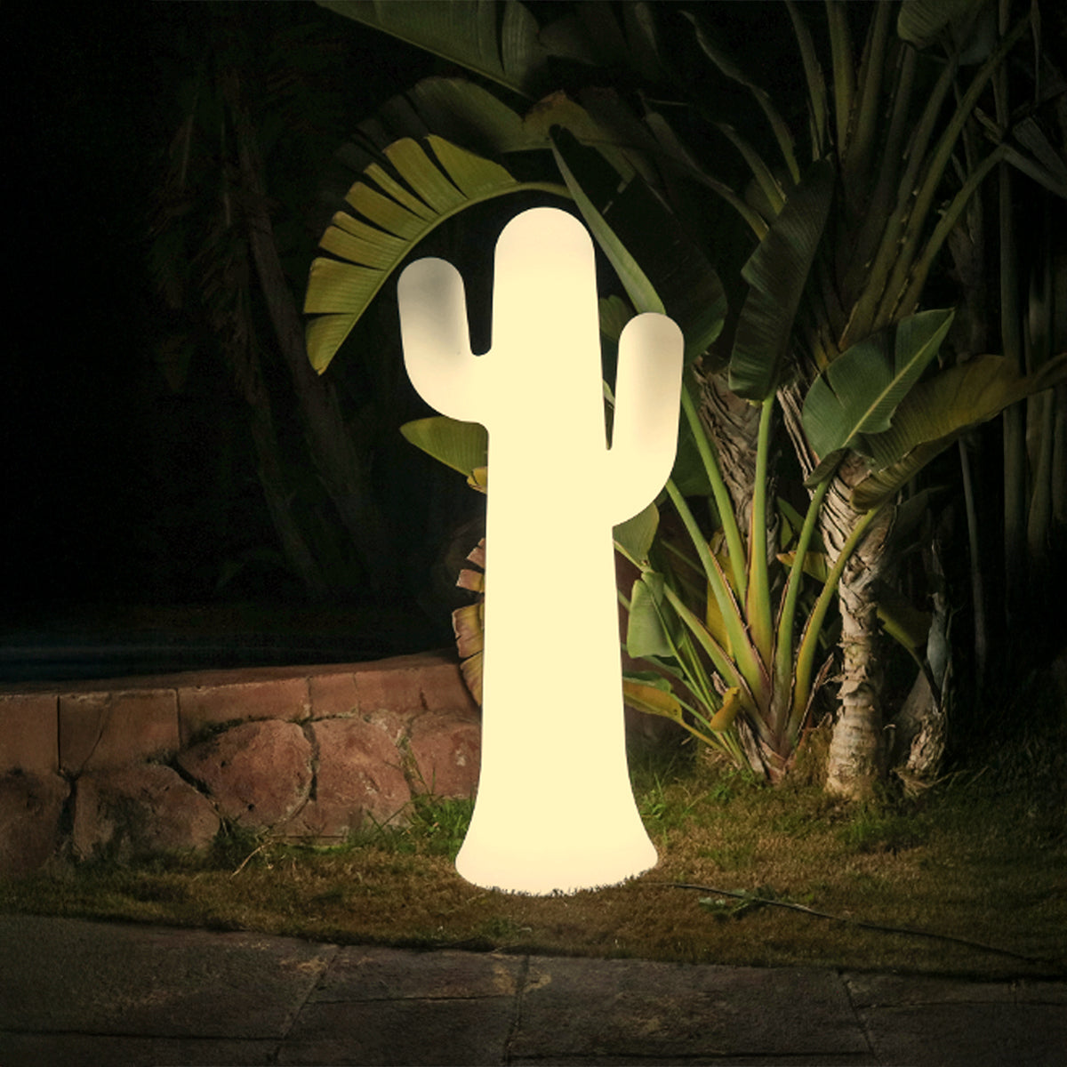 Cactus lumineux blanc allumé la nuit dans un jardin tropical, grandes feuilles vertes