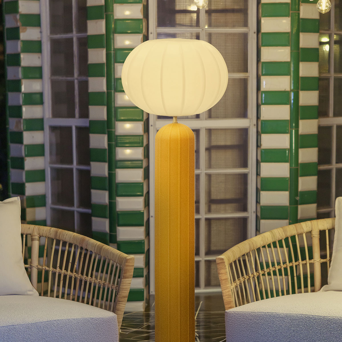 Lampadaire solaire allumé devant une façade à rayures vertes et blanches, entre deux fauteuils.