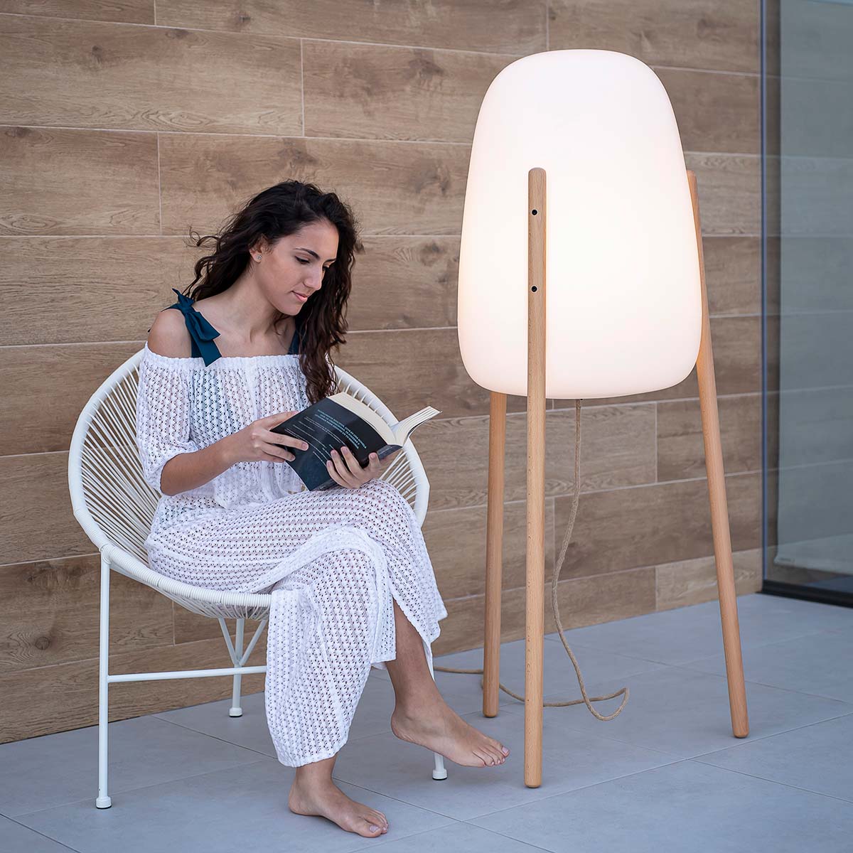 Femme lisant un livre assise dans un fauteuil, lampadaire allumé en intérieur bois