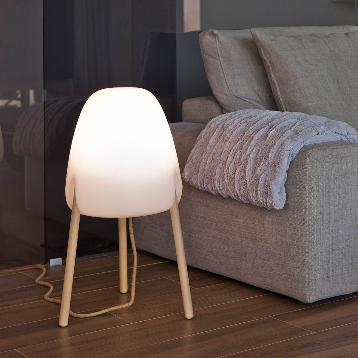Lampadaire blanc aux trois pieds en bois devant un canapé beige et une couverture