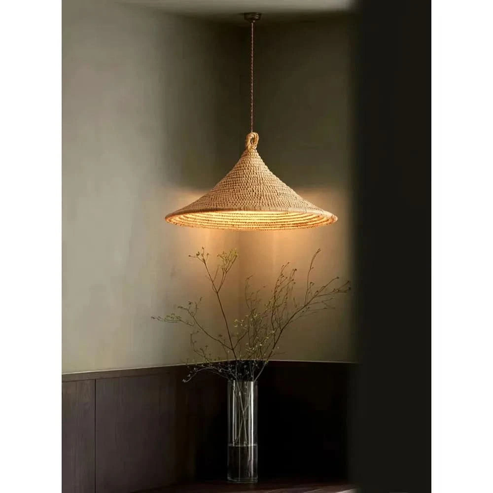 Luminaire suspendu allumé éclairant un vase transparent rempli de fines branches.