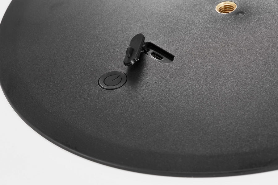 Détail du dessous : interrupteur, bouton et filetage doré sur matière noire texturée.