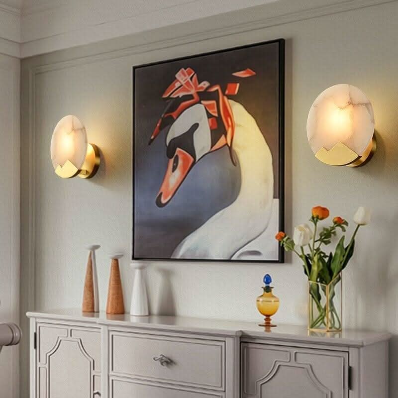 Deux appliques rondes encadrant un tableau de cygne au-dessus d'un buffet clair.