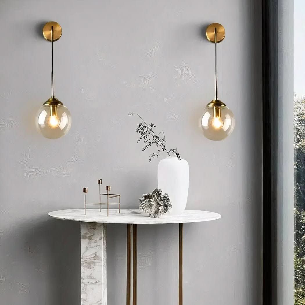 Deux appliques murales dorées avec boule de verre allumées au-dessus d'une console en marbre