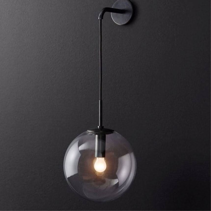 Applique murale noire, sphère de verre transparent et ampoule allumée sur fond gris.