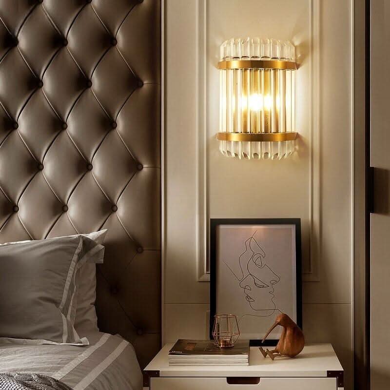 Applique murale cylindrique éclairée au-dessus d'une table de chevet près d'une tête de lit capitonnée.