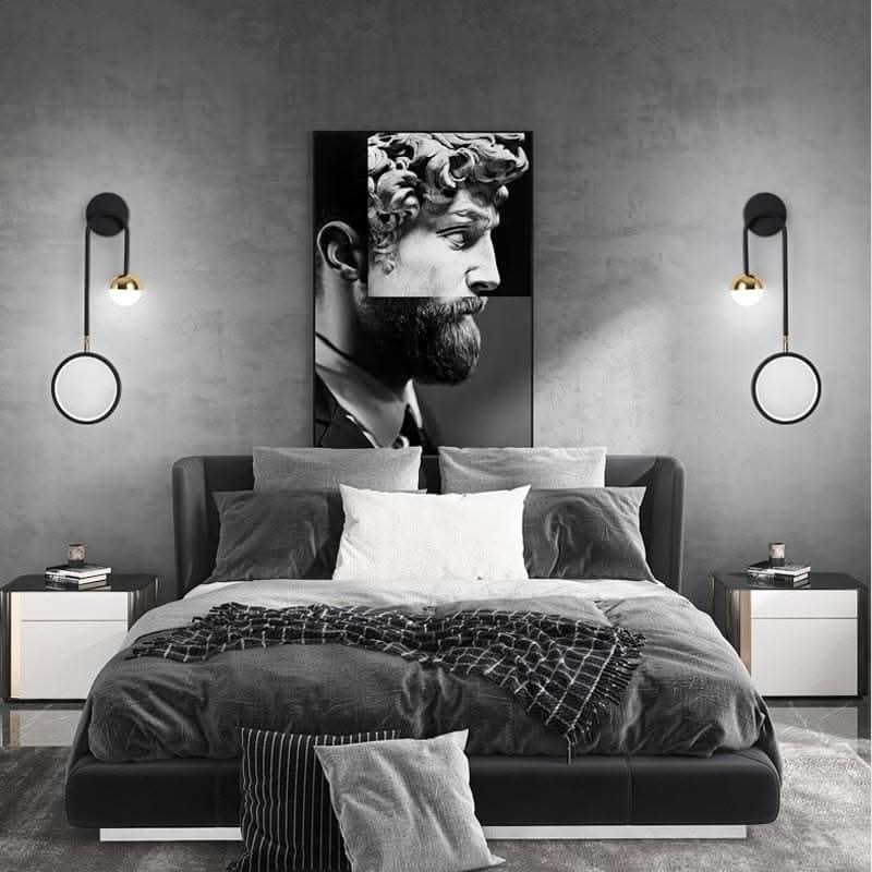 Deux appliques murales identiques encadrent un lit avec tête de lit, tableau et murs gris.