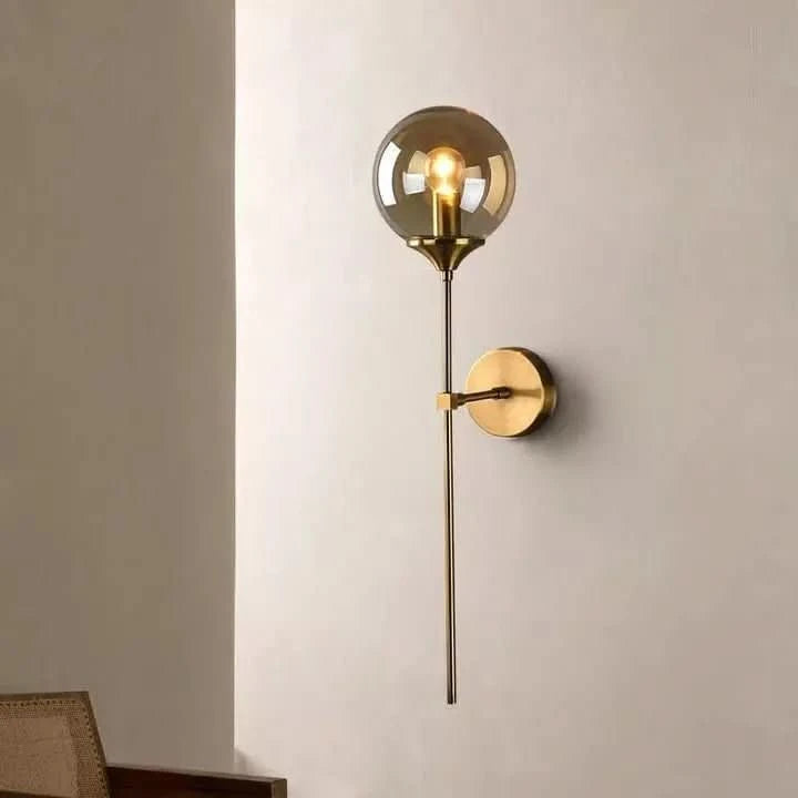 Luminaire mural doré allumé, installé sur un mur beige clair en intérieur.