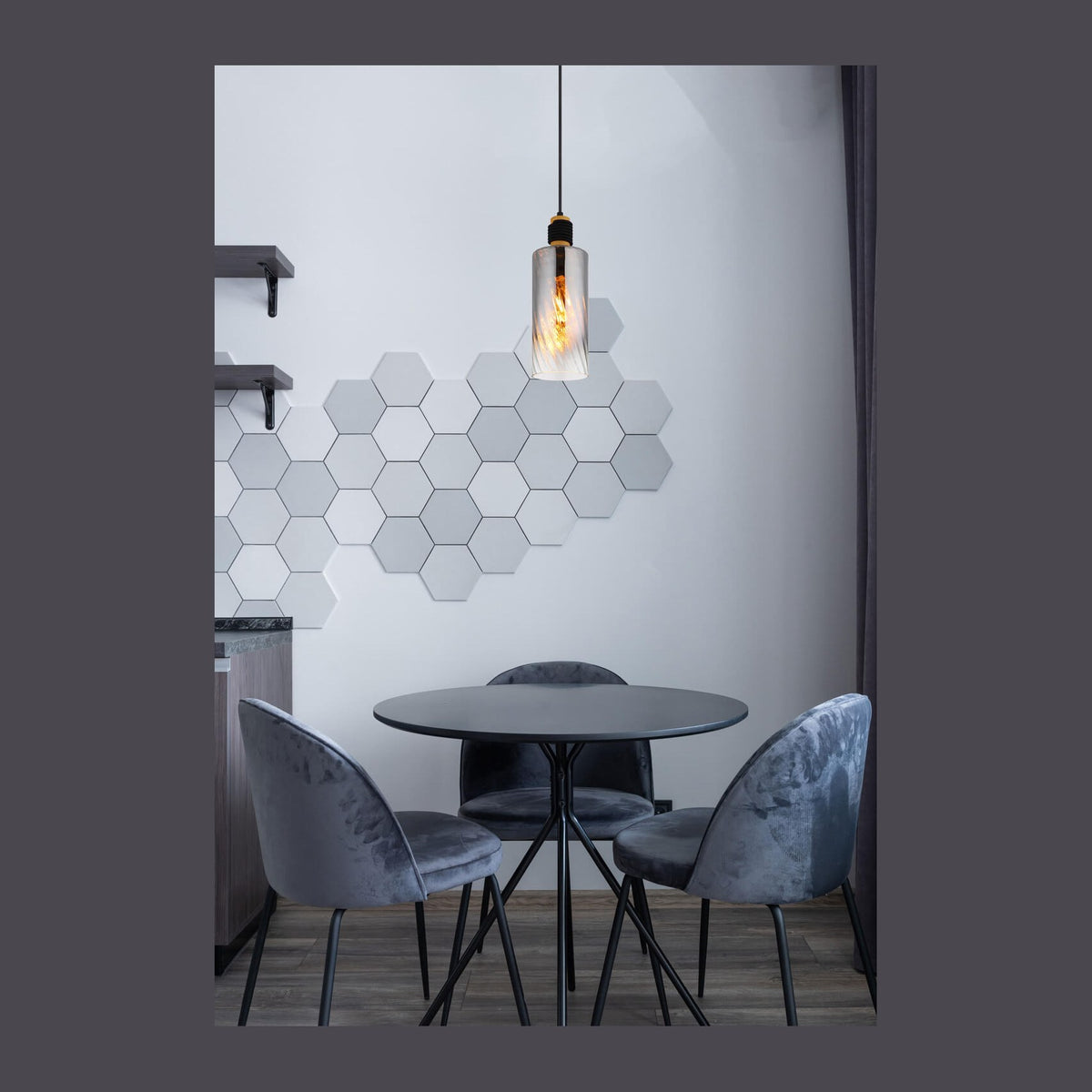 Suspension allumée au-dessus d'une table ronde, chaises en velours et déco murale hexagonale.