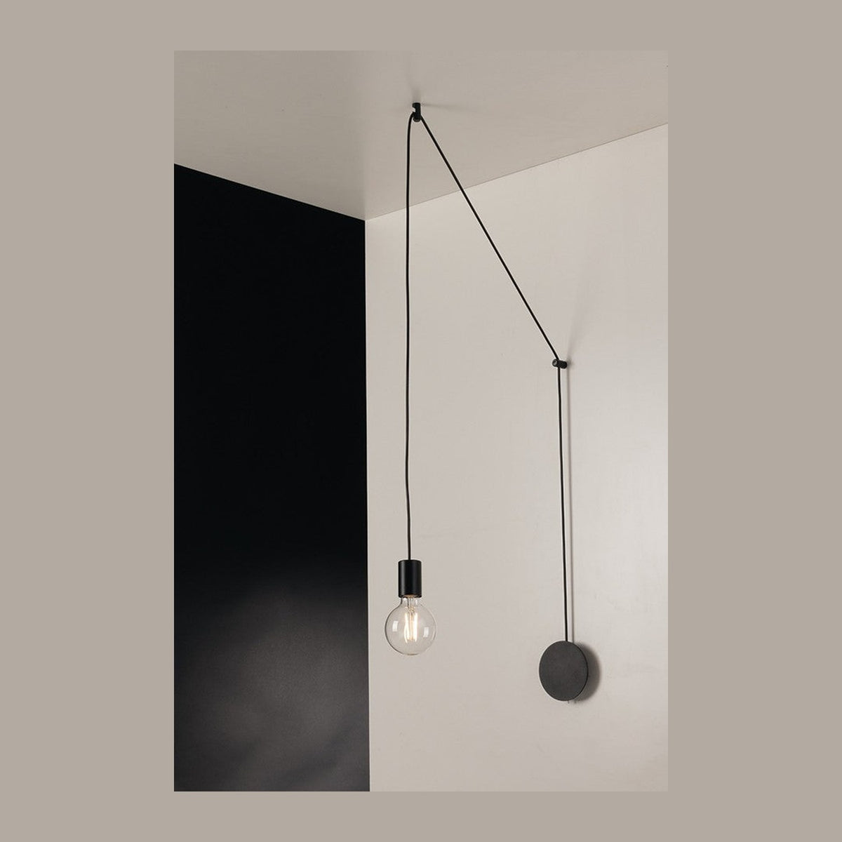Plafonnier noir suspendu, câble tendu entre plafond et mur, ampoule globe allumée